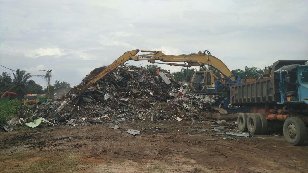 Excavator loading metal scrap into dump trucks